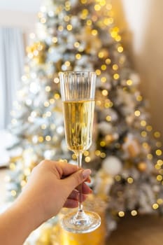 Champagne in a female hand against the background of Christmas tree lights. Selective focus. Festive day, atmospheric moment.