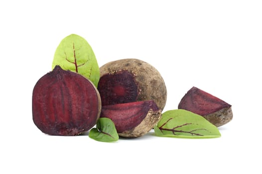 Slices of beetroot showing their purple interior arranged next to whole beetroots vegetables with their green leaves still attached isolated on white background