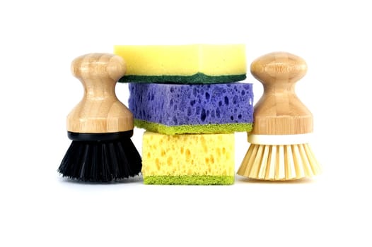Three sponges, each a different color purple, yellow, and blue and two brushes with wooden handles isolated on white background, cleaning tools