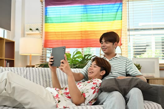 Loving young gay couple using digital tablet on couch. LGBT, love and lifestyle relationship concept.