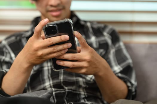 Smiling man using smartphone scrolling through the news feed in social media.