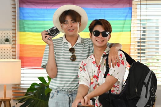 Happy young gay couple with analog camera and backpack get ready for a vacation trip.