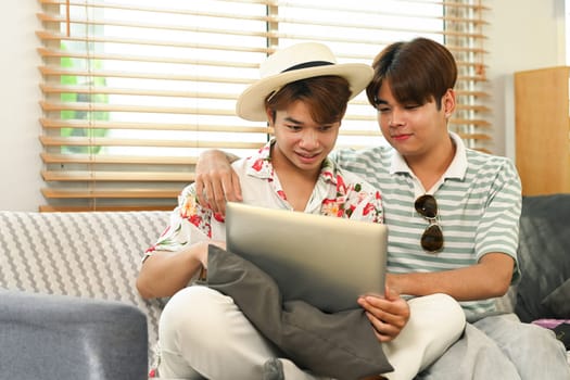 Gay male couple using laptop for searching travel destinations on website.