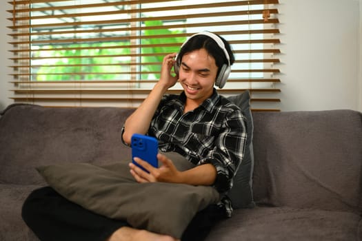 Cheerful asian man with wireless headphones enjoying his favorite music playlist on mobile phone.