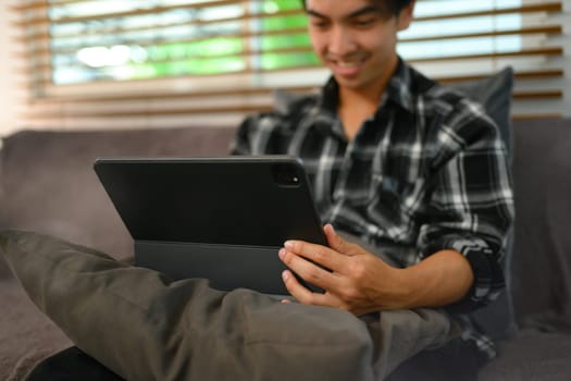 Selective focus. Hand of young man using digital tablet while sitting on couch at home.