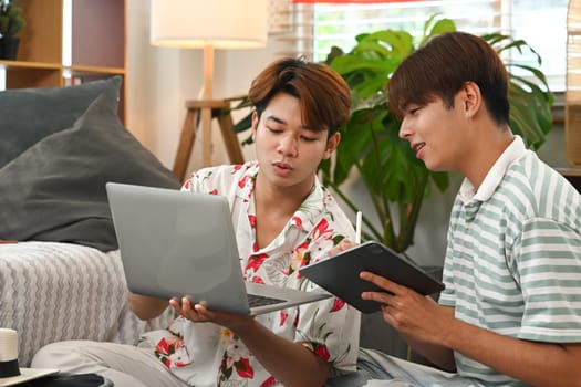 Happy young gay male couple planning vacation trip, using laptop for booking a hotel on website.