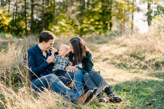 Mom hugs dad with a little girl sitting on his lap in a clearing. High quality photo