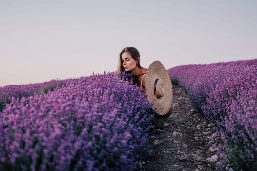 Close up portrait of young beautiful woman in a white dress and a hat is walking in the lavender field and smelling lavender bouquet.