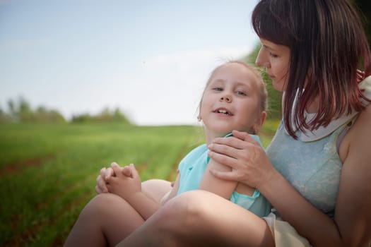 Happy mother and daughter enjoying rest, playing and fun on nature in green field. Woman and girl resting outdoors in summer or spring day