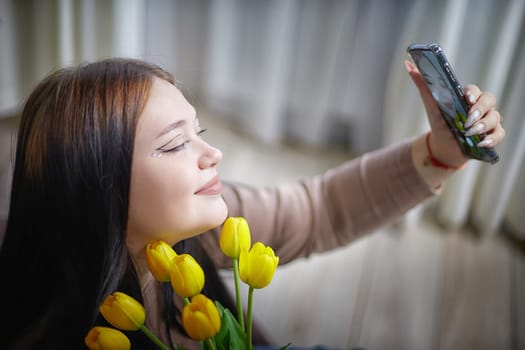happy stylish fat plumb brunette girl making selfie with yellow tulips in room. happy young lady on International women's day, young hipster woman