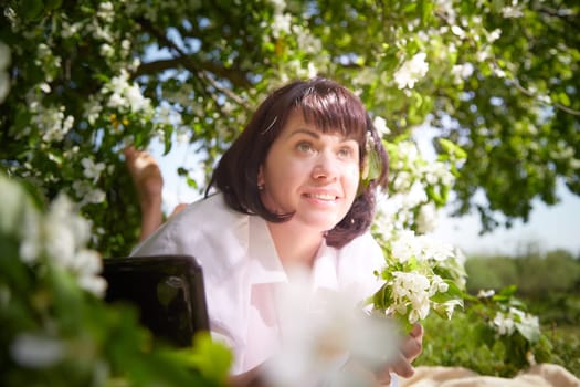 Girl walking, Relaxing near Blossoming apple Tree on Sunny Day. Portrait of Middle aged woman enjoying nature surrounded by white blossoms