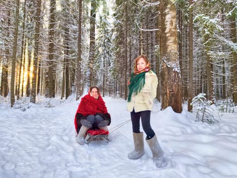 Mother and daughter in shawls are sledding in the winter forest. Ethnic clothes and fun on Shrovetide carnival Maslenitsa
