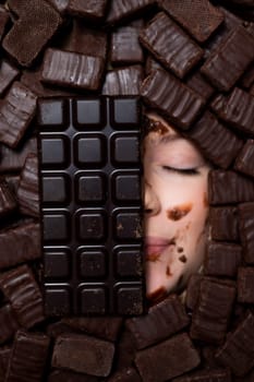 The face of a caucasian woman surrounded by sweets. The girl is smeared in chocolate