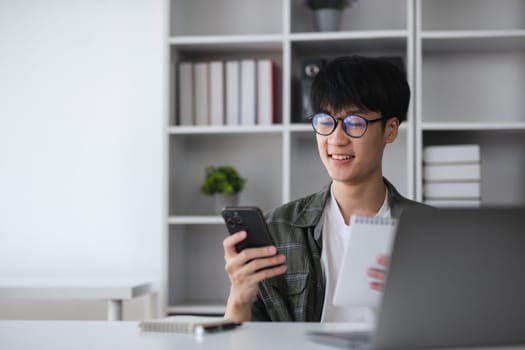 Young Asian student boy in private clothes studying online with laptop at home..