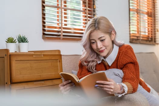 Beautiful Asian woman lying down and reading a book in the living room on vacation at home..