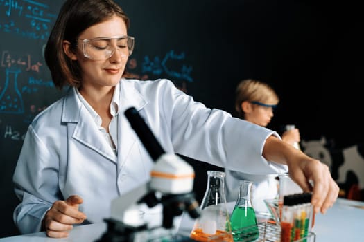 Teacher support schoolboy learning science of chemistry do experiment in laboratory wear lab coat and safety glasses in STEM class. Teacher manage test tube on the table with confidence. Erudition.