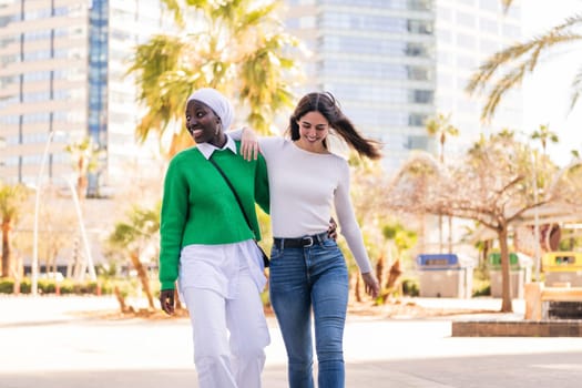 young multiracial couple of two women walking smiling happy through the city hugging, concept of diversity and modern lifestyle, copy space for text