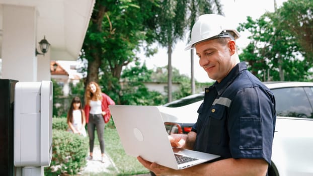 Qualified technician working on home EV charging station installation, making troubleshooting and configuration setup on charging system with laptop for EV at home. Synchronos