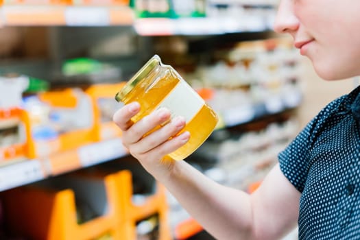 Young male hand holds honey on a blurred background, row of shelves with groceries in supermarket