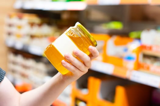 Young male hand holds honey on a blurred background, row of shelves with groceries in supermarket