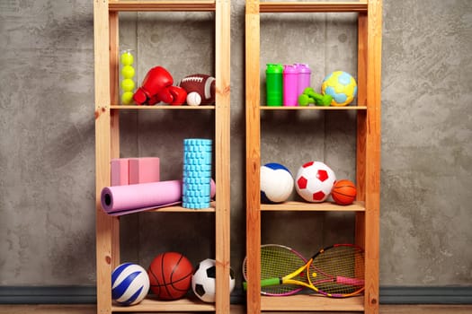 Shelves with different sports equipment against green wall close up