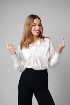 Young businesswoman standing against gray background and pointing her finger to copy space. High quality photo