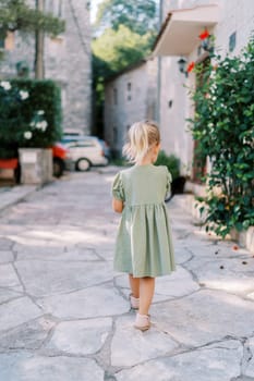 Little girl walks along a cobbled street past old stone houses. Back view. High quality photo