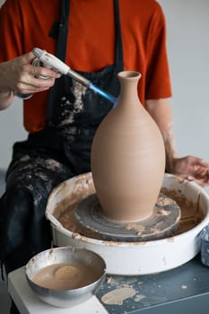 Close-up of a potter's hands firing a jug with a gas burner on a potter's wheel. Vertical photo