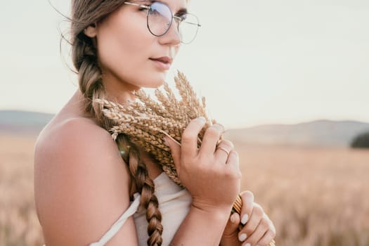 A woman is holding a bunch of wheat in her arms. The wheat is dry and brown, and the woman is wearing a white dress. The scene is set in a field, and the woman is posing for a photo