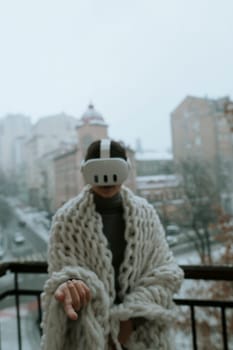 A young woman in a virtual reality headset stands on the balcony in winter. High quality photo