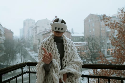 Immersed in virtual reality, a girl wears a VR headset on the balcony during winter. High quality photo