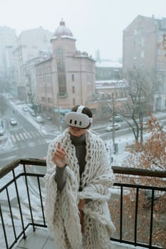 Winter chill meets virtual thrills as a young woman wears a VR headset on the balcony. High quality photo