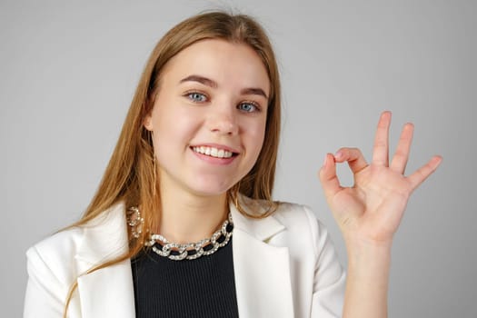 Confident Young Woman in Business Attire Giving Ok Sign in Studio Setting close up