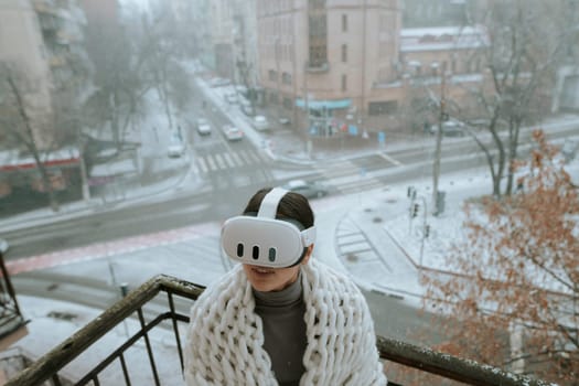 Immersed in virtual reality, a girl wears a VR headset on the balcony during winter. High quality photo