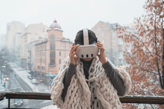 A charming woman in VR glasses marvels at the winter city scene around her. High quality photo