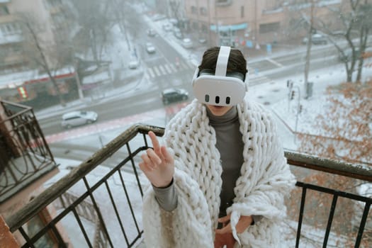 A girl immerses herself in virtual reality on the winter balcony, wearing a headset. High quality photo