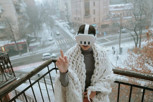 Amidst snowy landscapes, a young lady enjoys VR on the balcony with a headset. High quality photo