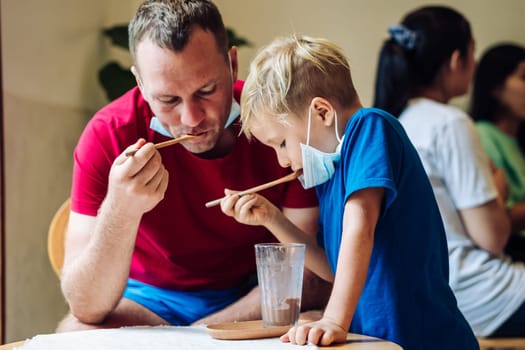 Father and son eat chocolate dessert with spoons in Cafe. Spending time together. Sweet tooth. Happy childhood.