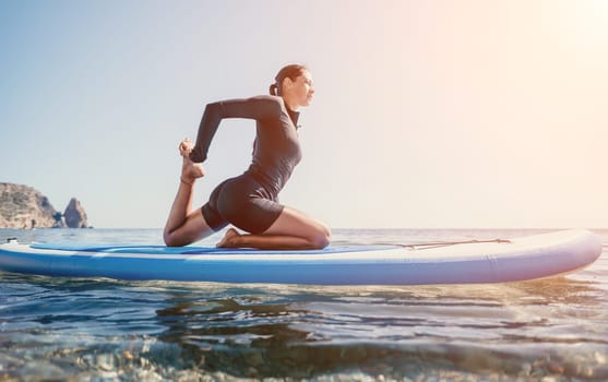 Woman sup yoga. Middle age sporty woman practising yoga pilates on paddle sup surfboard. Female stretching doing workout on sea water. Modern individual hipster outdoor summer sport activity