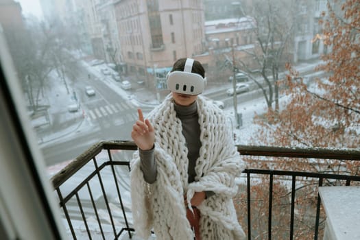 On the balcony in winter, a girl embraces virtual reality adventures with a headset. High quality photo