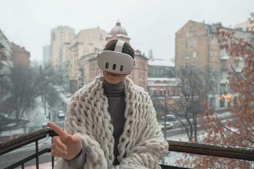 Enjoying VR experiences, a young lady dons a headset on the winter balcony. High quality photo