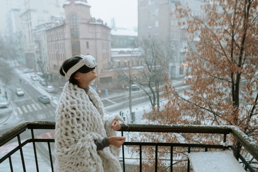 A beautiful girl in virtual reality glasses against the backdrop of a winter cityscape. High quality photo