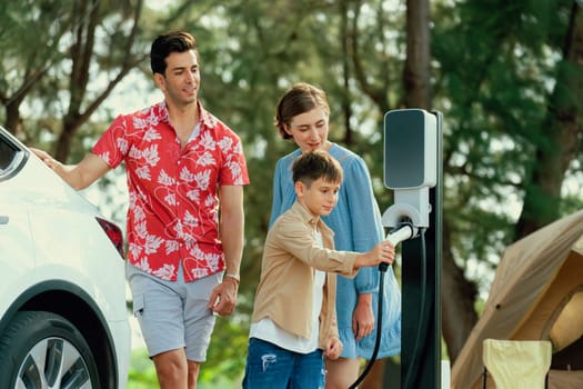 Outdoor adventure and family vacation camping in nature travel by eco friendly car for sustainable future. Lovely family recharge EV car with EV charging station in campsite. Perpetual