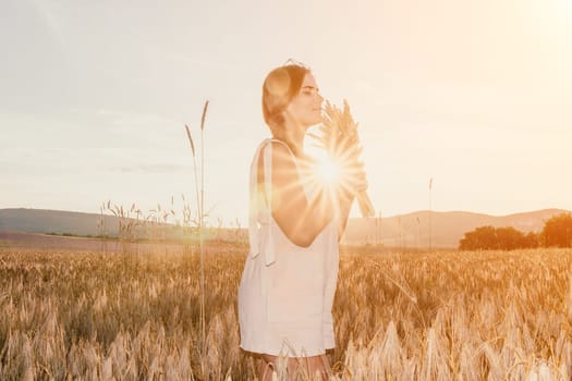 A woman is holding a bunch of wheat in her arms. The wheat is dry and brown, and the woman is wearing a white dress. The scene is set in a field, and the woman is posing for a photo