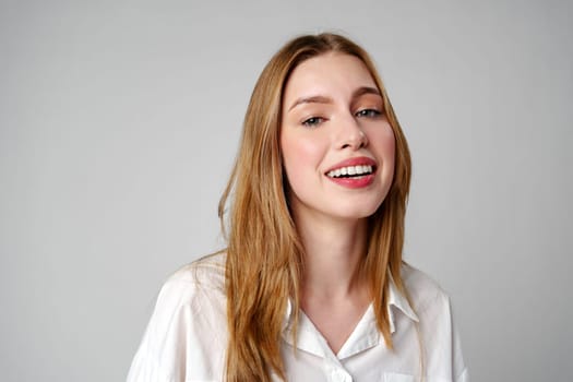 Joyful Young Blonde Woman Smiling against gray background in studio