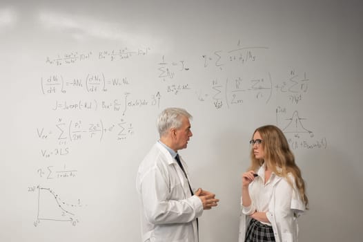 An elderly man and a young woman at a white board. Colleagues scientists discuss work issues