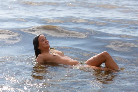 Young beautiful woman posing nude on the seaside enjoying the sea and nature