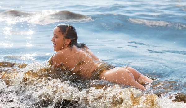 Young beautiful woman posing nude on the seaside enjoying the sea and nature