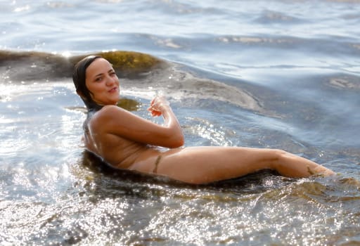 Young beautiful woman posing nude on the seaside enjoying the sea and nature