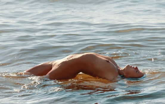 Young beautiful woman posing nude on the seaside enjoying the sea and nature